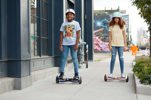 Two children riding the GOTRAX Glide Chrome Bluetooth Hoverboard with LEDs