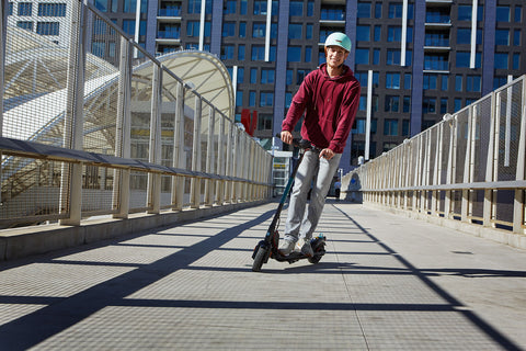 Man riding GOTRAX Apex Electric Scooter on a paved path in a city.