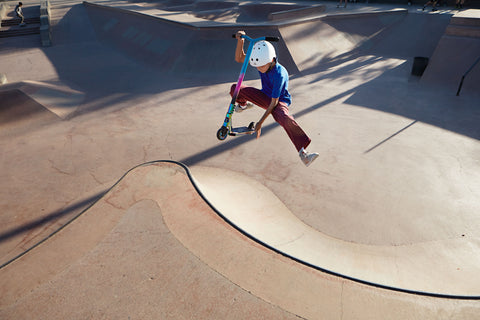 Child performing a trick on a RideVolo T03 Stunt Scooter for Kids at a skate park