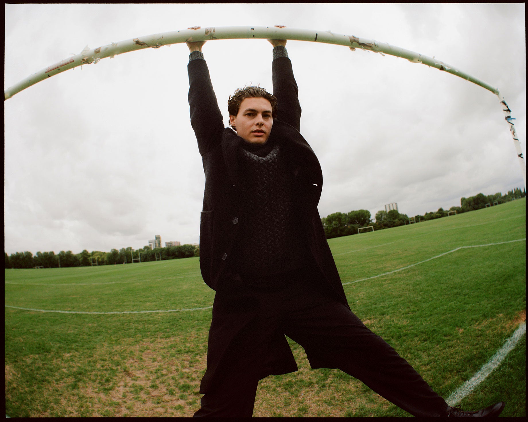 Model wearing Wax London outfit hanging from goal posts on football pitch