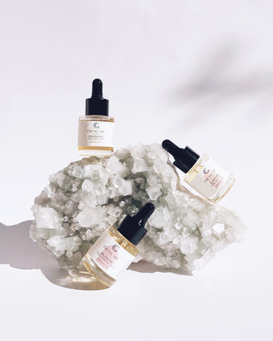 three dropper bottles of facial oil balancing on a crystal