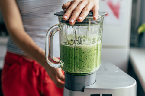woman making green juice in electric mixer