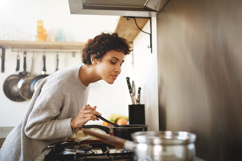 woman stirring pan while enjoying the scent of spices