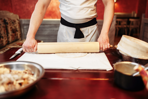 A lady rolling out some pastry on the board