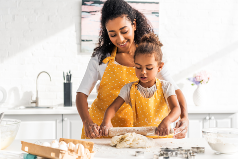 A mom and daughter wearing matching yellow aprons rolling dough together