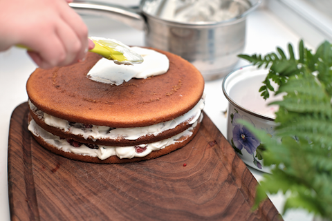 A chocolate cake being frosted with vanilla icing using a yellow spatuala 