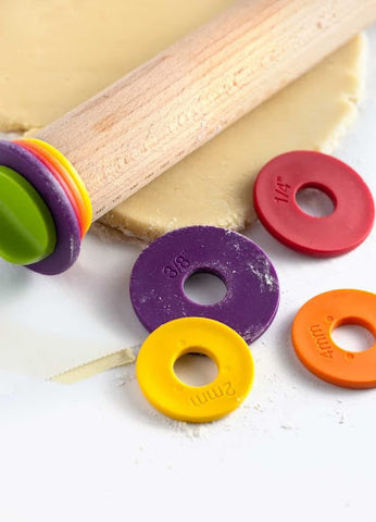 A wooden rolling pin with multi colored disks sitting on the pastry