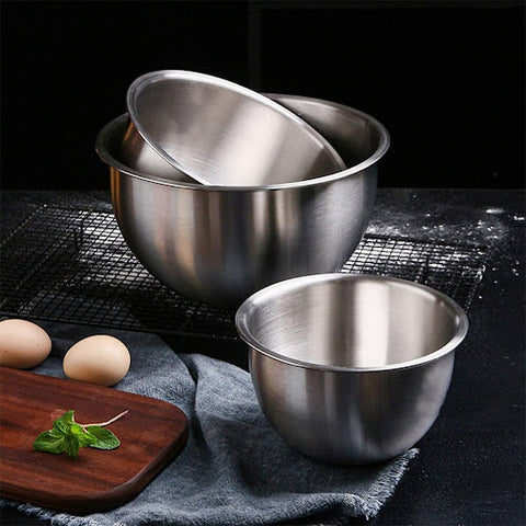 Three silver mixing bowls on a black kitchen surface with two eggs, a chopping board and mint