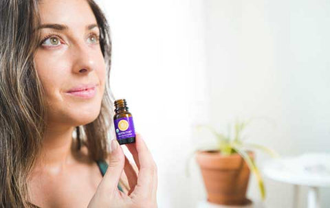 woman holds open bottle of Protector essential oil blend inhaling the aroma