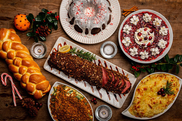 holiday table full of desserts, challah, prime rib, and casseroles