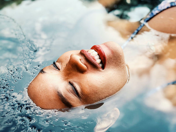 woman laying in water with her face above the water, she is smiling with eyes closed