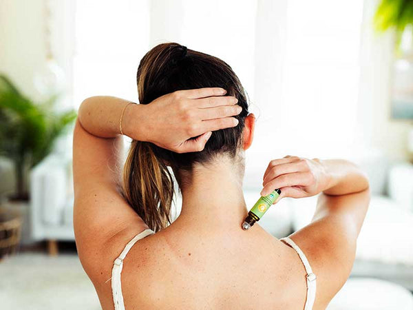 woman applies muscle relief essential oil roll-on to the back of her neck