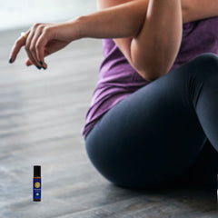 woman sitting on the floor and stretching with peppermint roll-on next to her