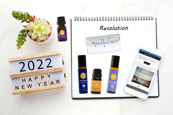 desktop showing calendar 2021 happy new year, mobile phone with meditation audio featured on screen, a succulent, essential oils and notepad that says resolutions: mindfulness