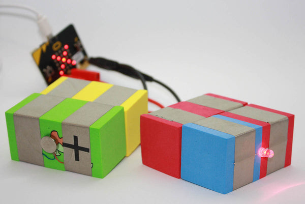 On the left a vibration TapeBlock with a TapeBlock connecting to a cable and banana plug, attached to a Micro:bit and on the right a LED TapeBlock connecting to a cable and banana plug, attached to the same Micro:bit which is in the background