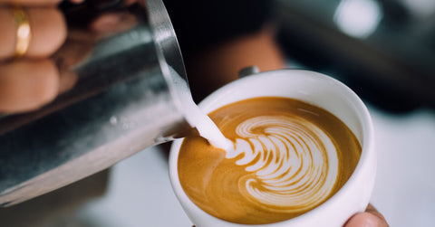 a person pouring a latte to a coffee cup