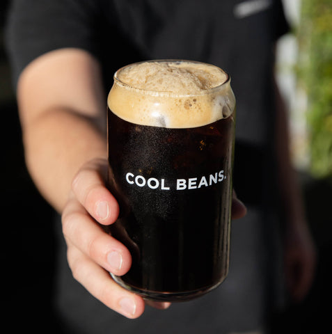 Person holding Cool Beans glass filled with cold brew.
