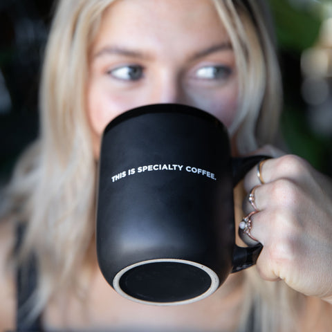 person drinks coffee out of coffee mug that reads "This is Specialty Coffee"