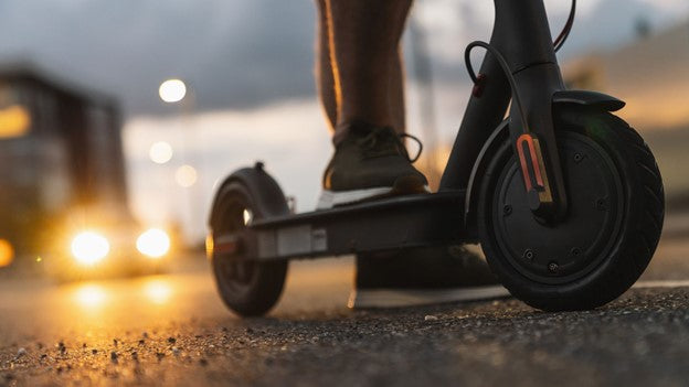 Person riding rideo e scooter at road side and car coming from behind