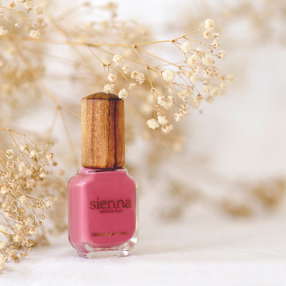 pink nail polish bottle with timber cap by sienna with baby's breath flowers background