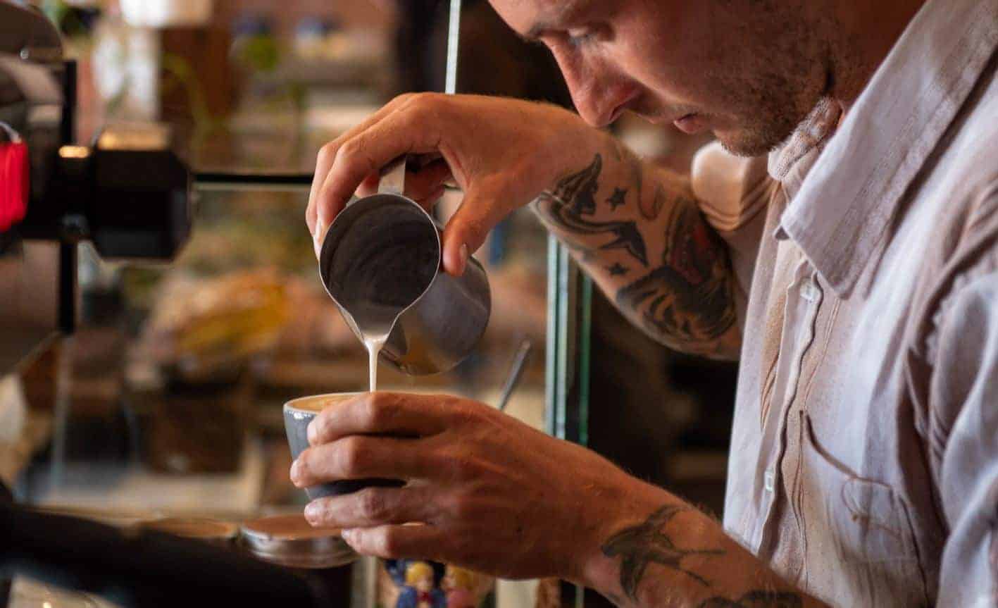 barista pouring milk in a coffee