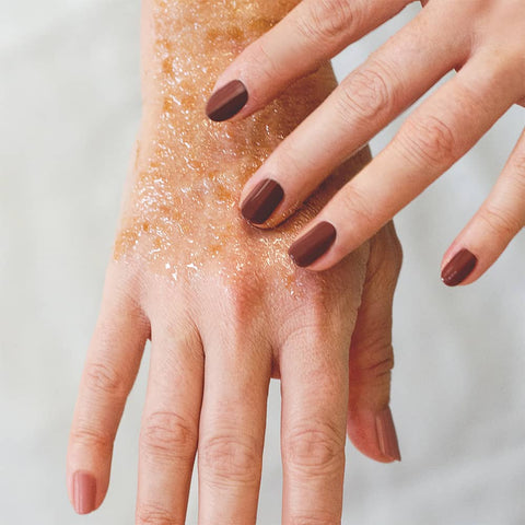 Hands applying a Coconut Scrub Vegan Face Mask wearing deep brown nail polish by sienna