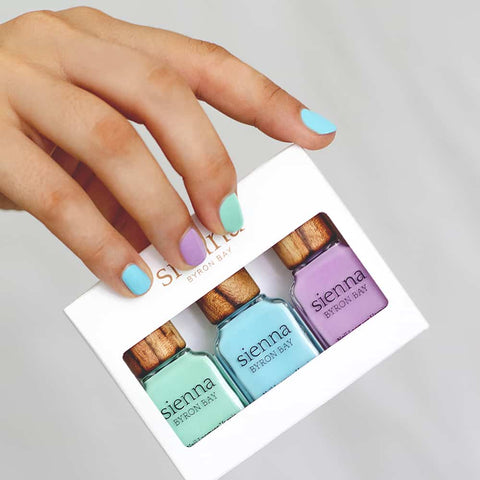 Hand holding a pack of three pastel green blue and purple nail polish by sienna