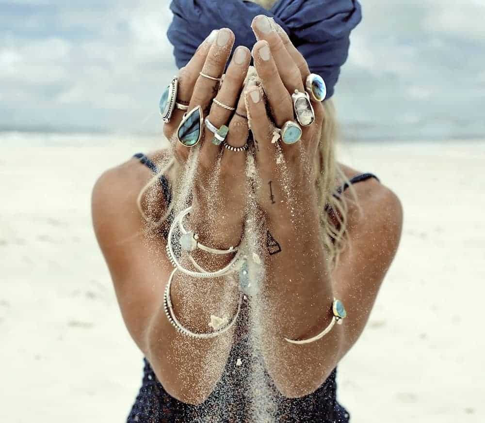 woman holding sand on a beach wearing kokopilli jewellery