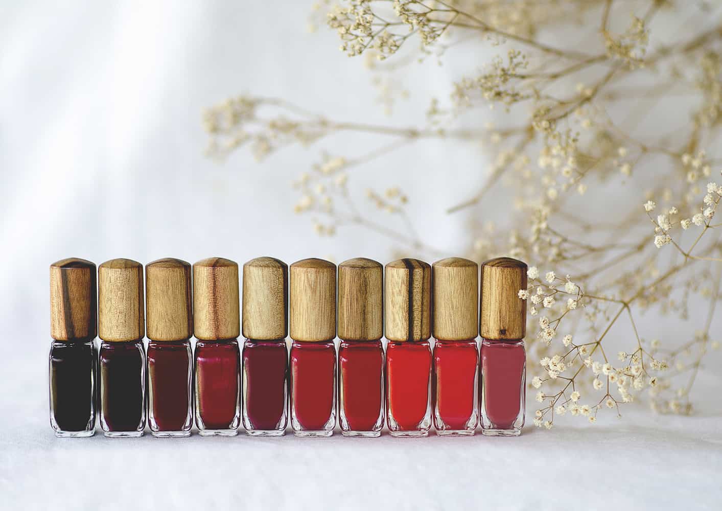 10 different red nail polish bottles with timber cap by Sienna with baby's breath flower background