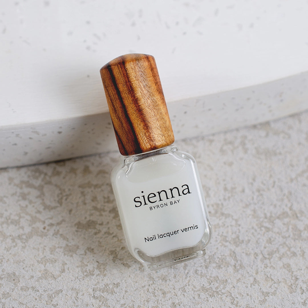 nail strengthener glass bottle with timber cap by sienna laid on the edge of a ceramic plate and concrete background