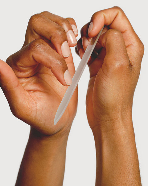 Medium brown skin hands using glass nail file on hands.