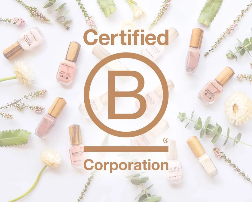 B-Corp logo over pink nail polish bottles with timber cap by sienna and white and pink flowers