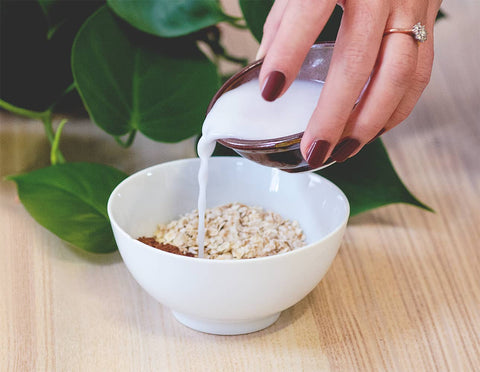 Hand pouring coconut milk in Cacao Brightener Vegan Face Mask by Sienna