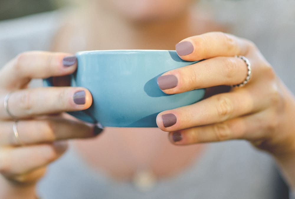 close view of hands holding a pale blue coffee cup wearing a Dusty mauve nail polish by sienna