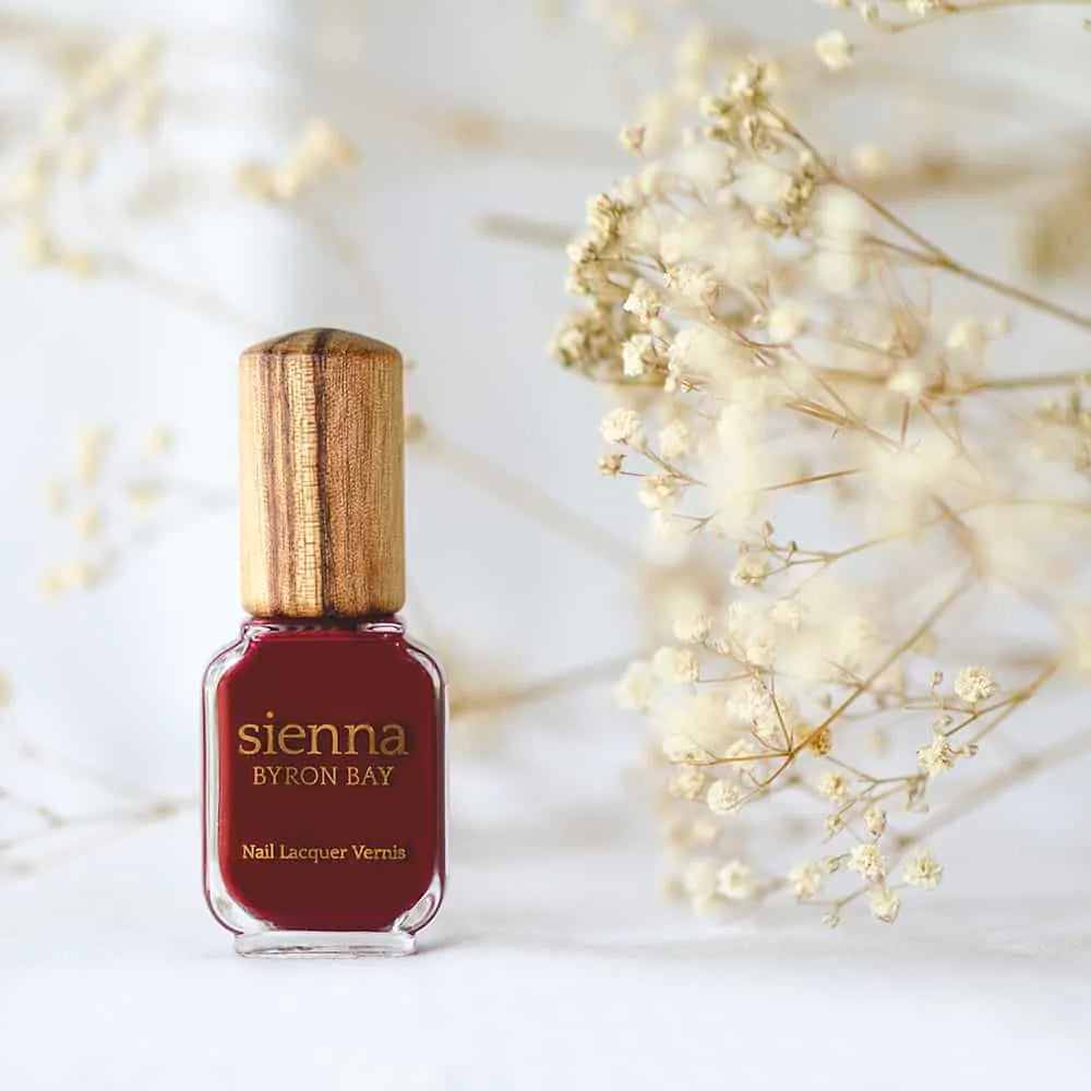 Organic mid-tone red nail polish bottle with timber cap by Sienna with baby's breath flower background