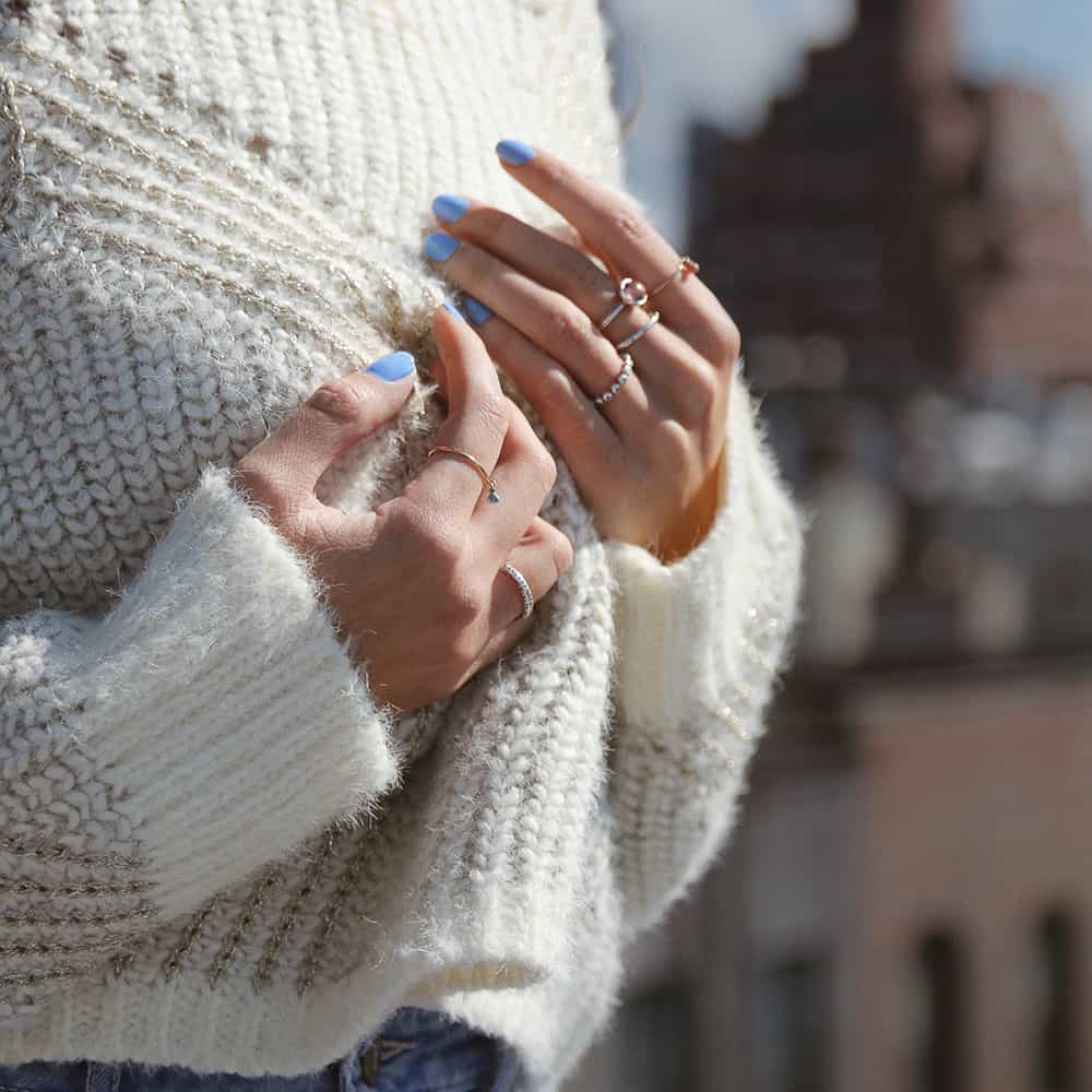 woman on top of a roof in New York holding her hands to her chest wearing a white knitted sweater and Light Periwinkle Blue nail polish by sienna