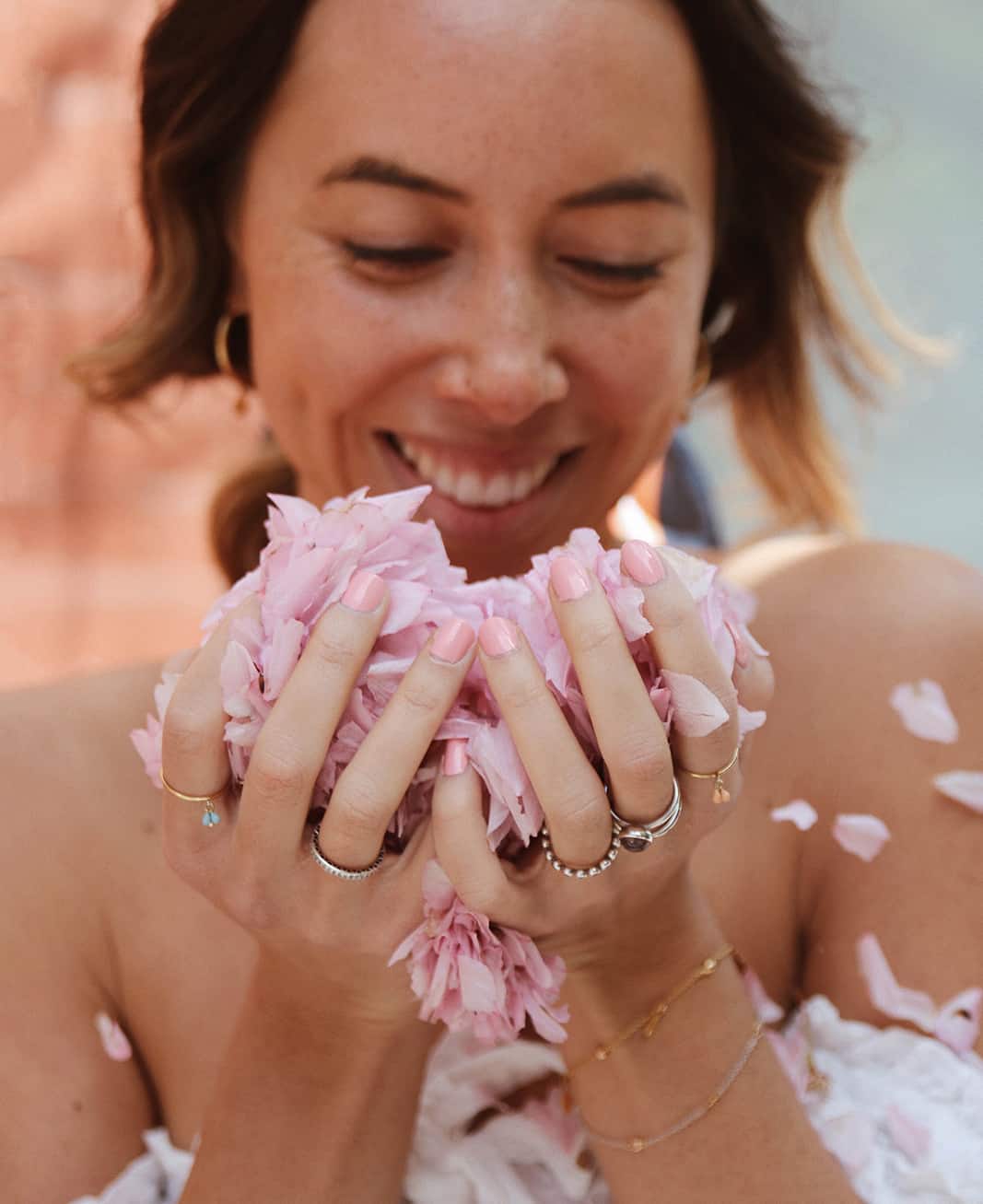 close view of a young woman's hands holding pink flower petals and wearing Cherry blossom pink nail polish by sienna