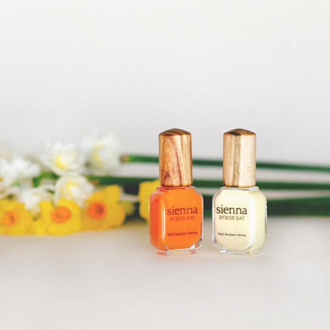 orange and pastel yellow nail polish glass bottle with timber cap by sienna with orange and yellow flowers in the background