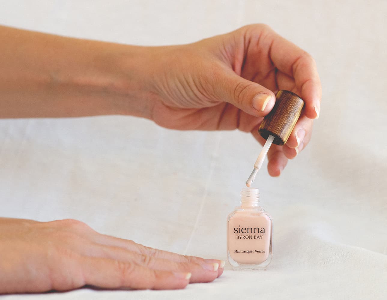 Hands applying nude pink nail polish by sienna