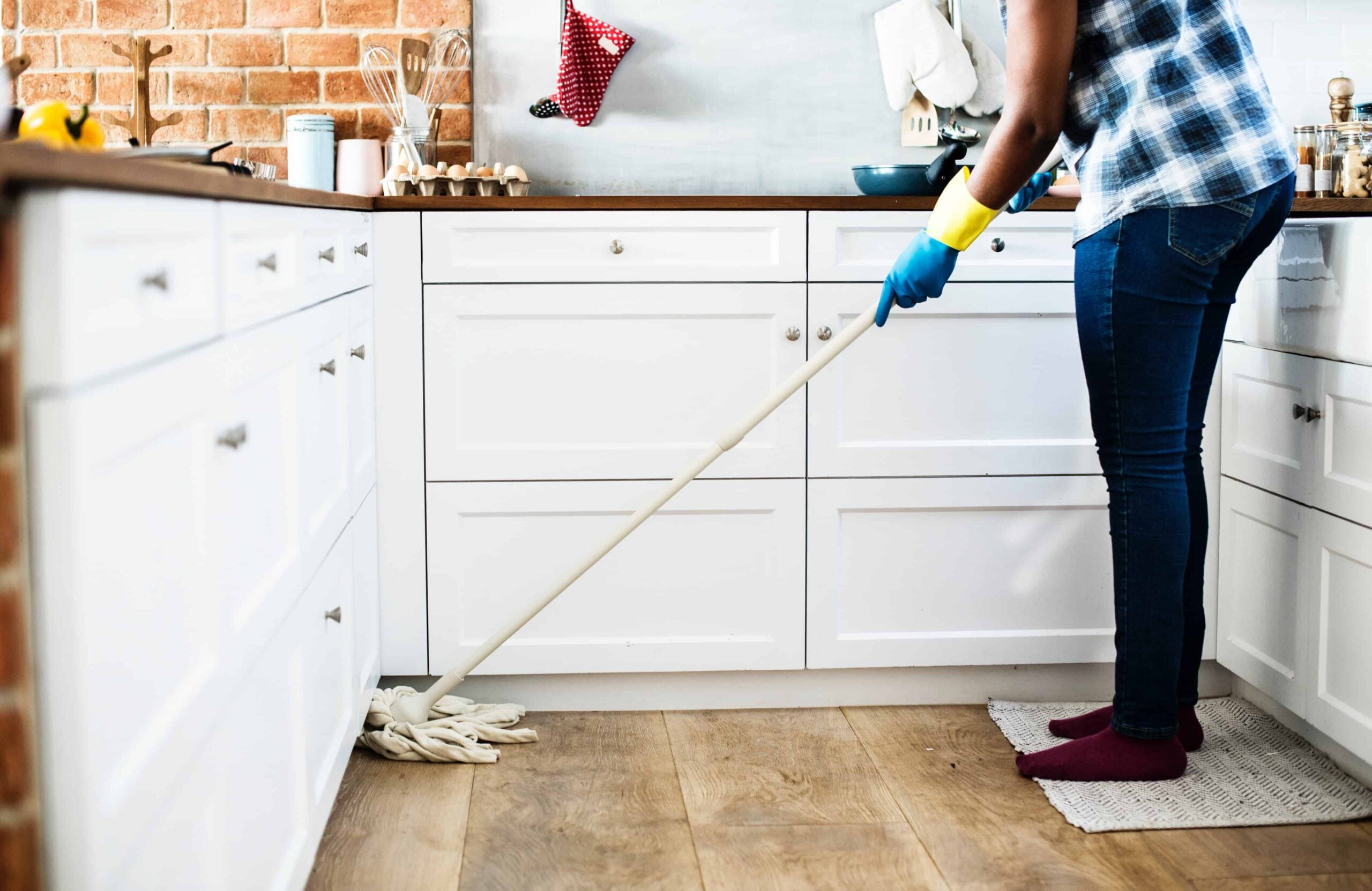 woman sweeping her kitchen floor wearing plastic gloves