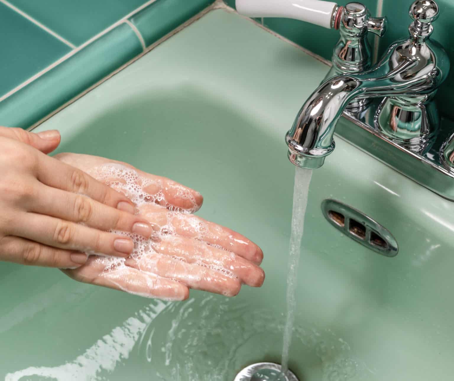 washing hands with soap in pastel green sink under running water