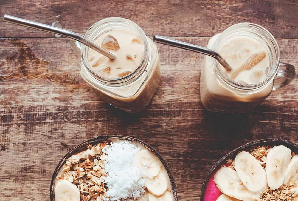 top view of ice coffees with metal straws and breakfast bowls on a wooden table