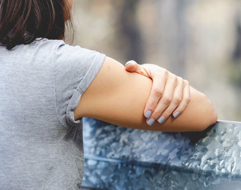 close view of woman holding her arm wearing a grey t-shirt and marble grey nail polish by sienna