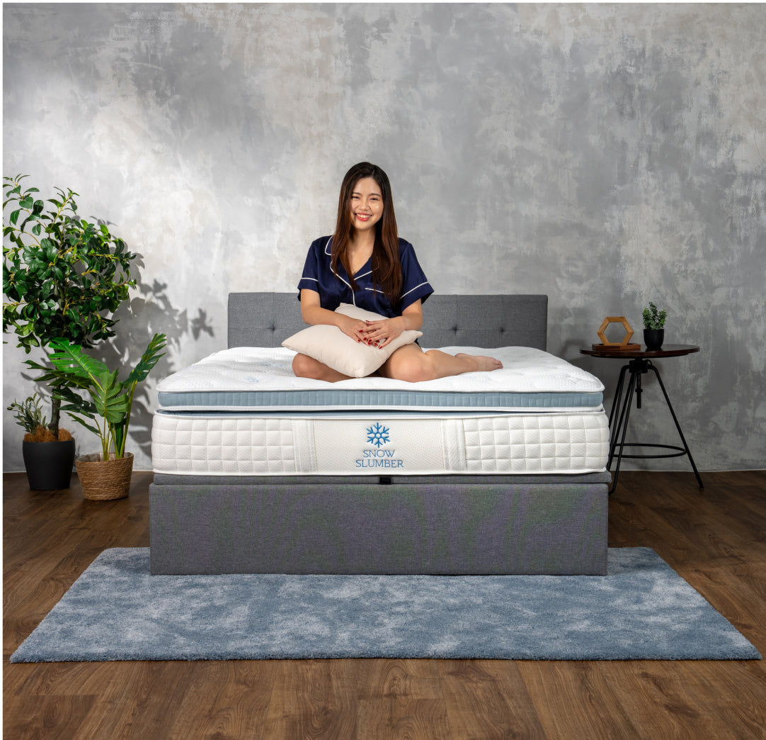 Person sitting on a bed with a Snow Slumber mattress in a cozy bedroom setting.