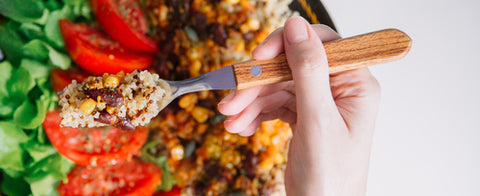 Top view of Female hands at dinner table holding fork above plate with quinoa, red beans, corn, tomato and green salad