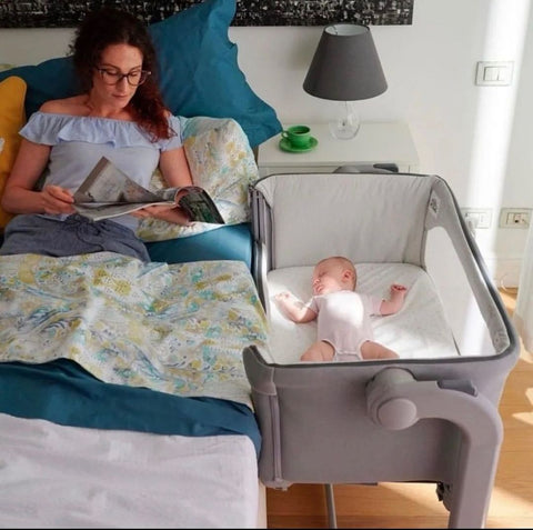 Dete u kolevci spava dok majka na kreveti čita knjigu