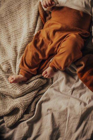 Bebi se vide samo nogice kako leži na posteljini od kašmira