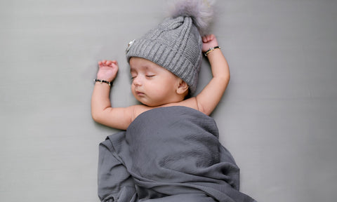 Beba sa sivom kapom spava i pokrivena je sivim pokrivačem