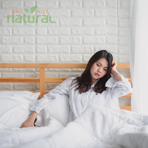 A woman in bed holding her head, looking tired and weak.