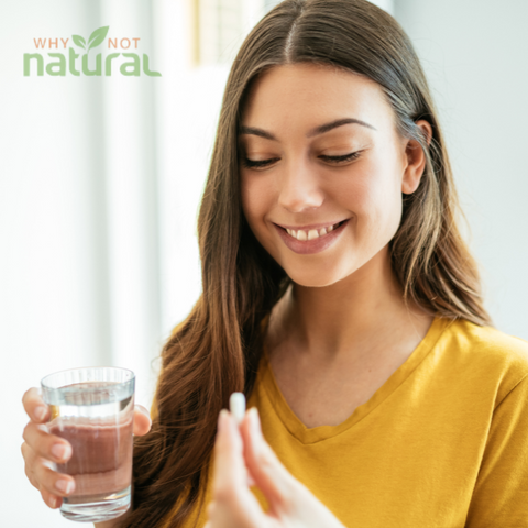 Woman holding a glass of water and a pill, taking a supplement.